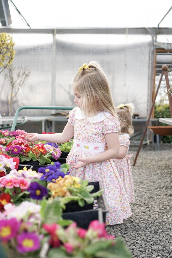 Toddler sisters in spring floral smocked dresses looking at flowers in a garden center 