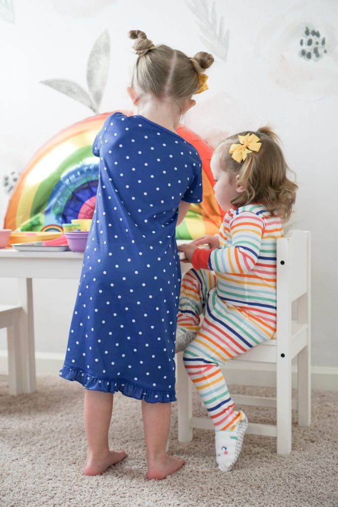 Toddler sisters playing with playdoh at a little white table with rainbow details in their Carter's rainbow pajamas. 