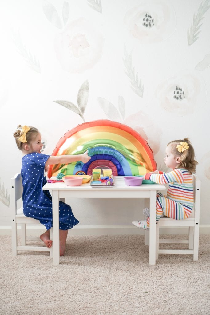 Toddler sisters playing with playdoh at a little white table with rainbow details in their Carter's rainbow pajamas. 