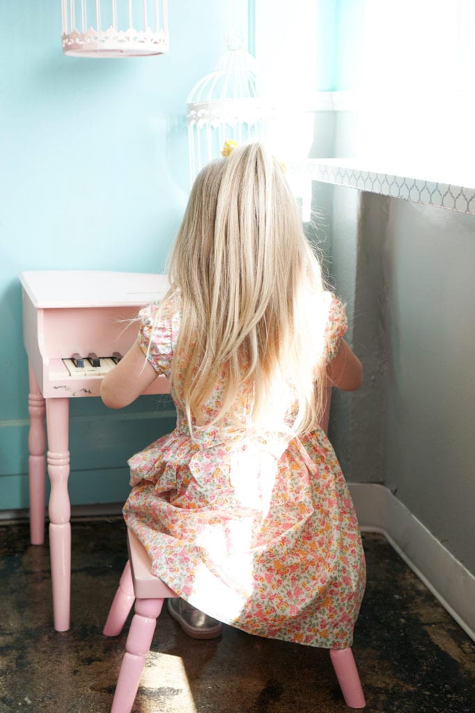 Toddler girl in a spring floral smocked dress sitting at a pink piano.