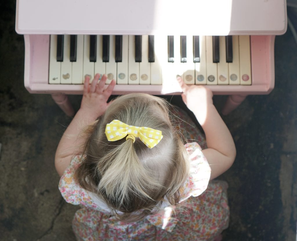 Baby girl with yellow bow sitting at a pink piano. 