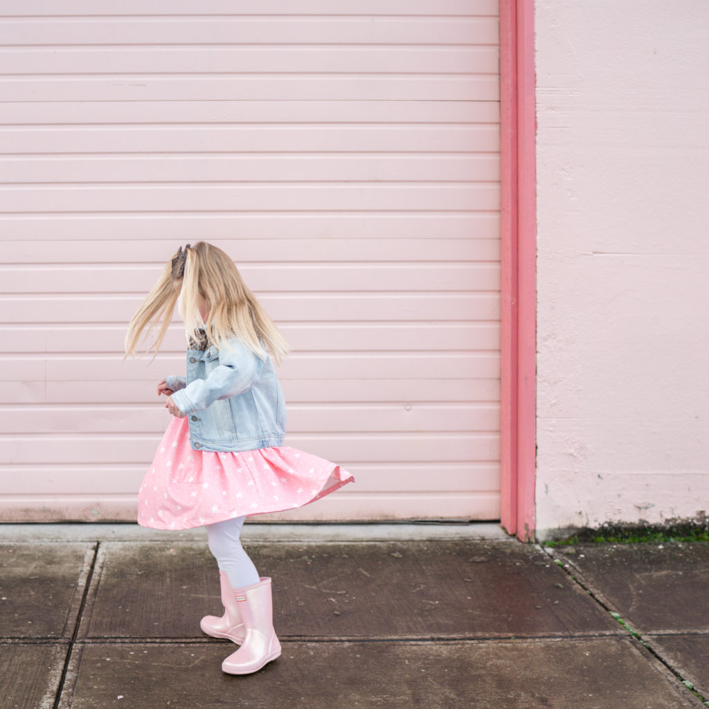 girl twirling in pink dress in front of pink wall