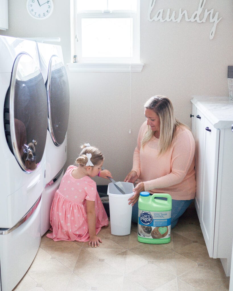 girl and mom helping clean cat box in laundry room 