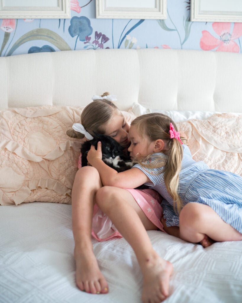 girls hugging cat on bed