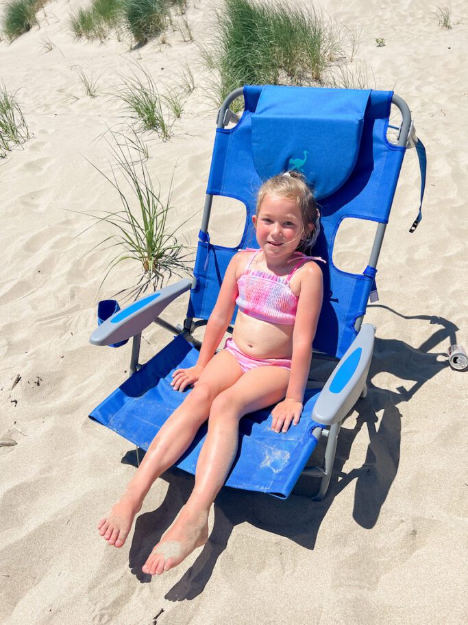 little girl sitting in blue beach chair on the beach